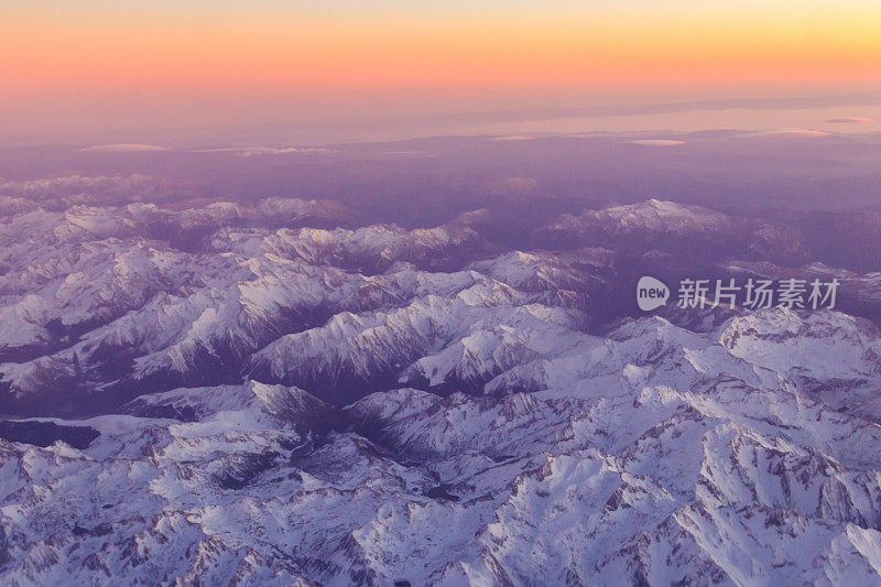 View out of an airplane window of a snow-covered mountain range at sunset